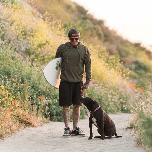 A surfer with his dog wearing a Kuthro baja premium dog leash walking to the beach.